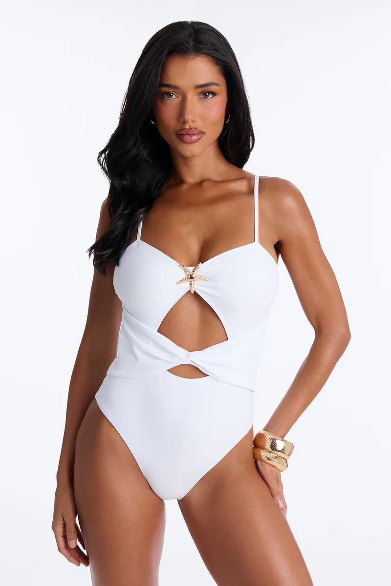 Stylish woman models white cut-out monokini with gold starfish detail & bangles. Perfect women's beach & resort swimwear.