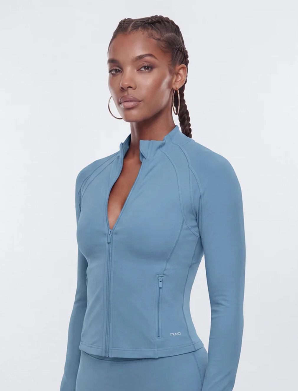 Woman in a slate blue, slim-fit zip-up athletic jacket with high collar, showcasing stylish women's activewear against a white background.