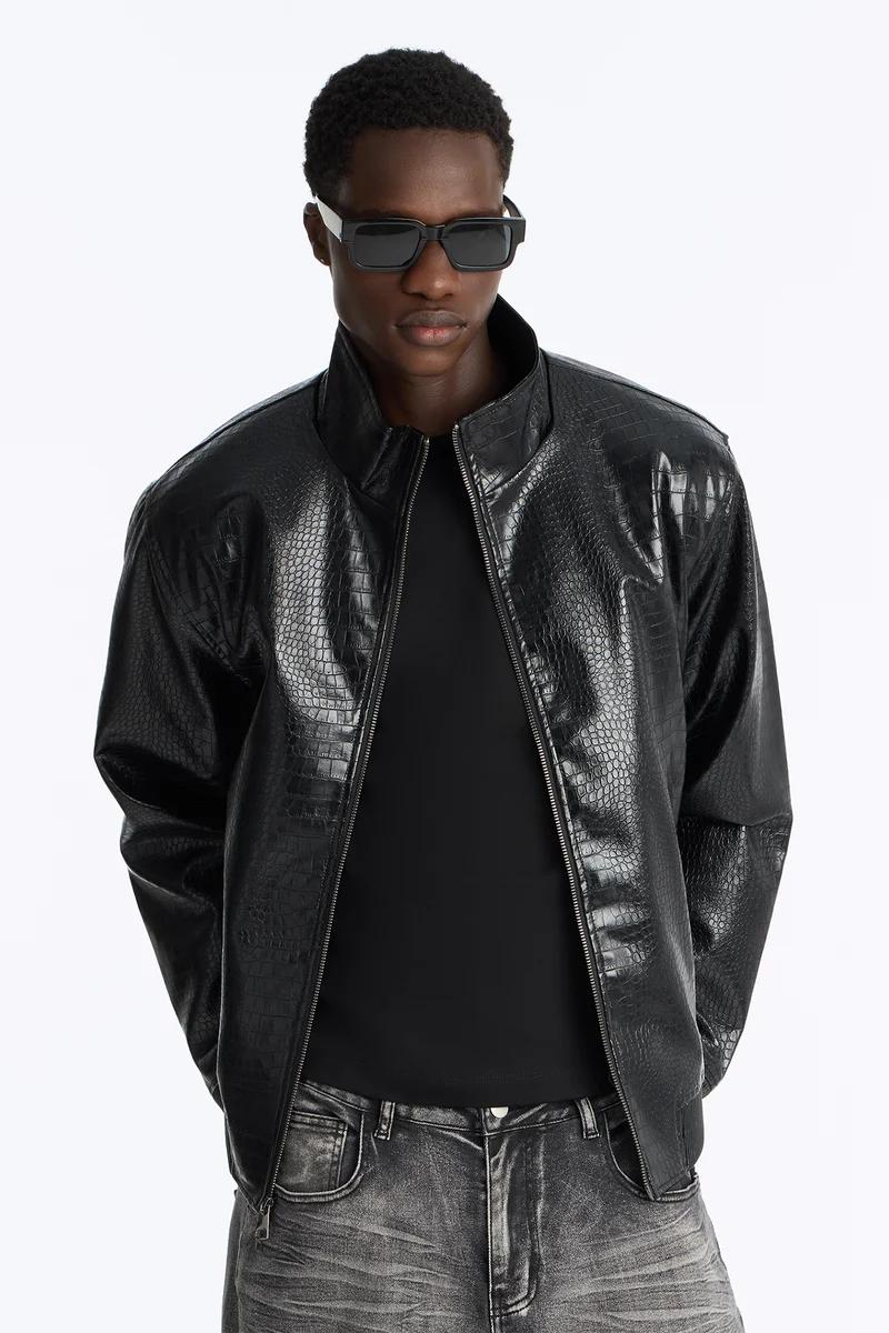 Man in stylish black faux leather bomber jacket with crocodile texture, black t-shirt, acid wash jeans, and sunglasses, showcasing new men's fashion.