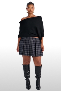 Modelo con suéter negro sin hombros, falda tableada de cuadros grises y botas altas, destacando la nueva colección de moda de otoño.