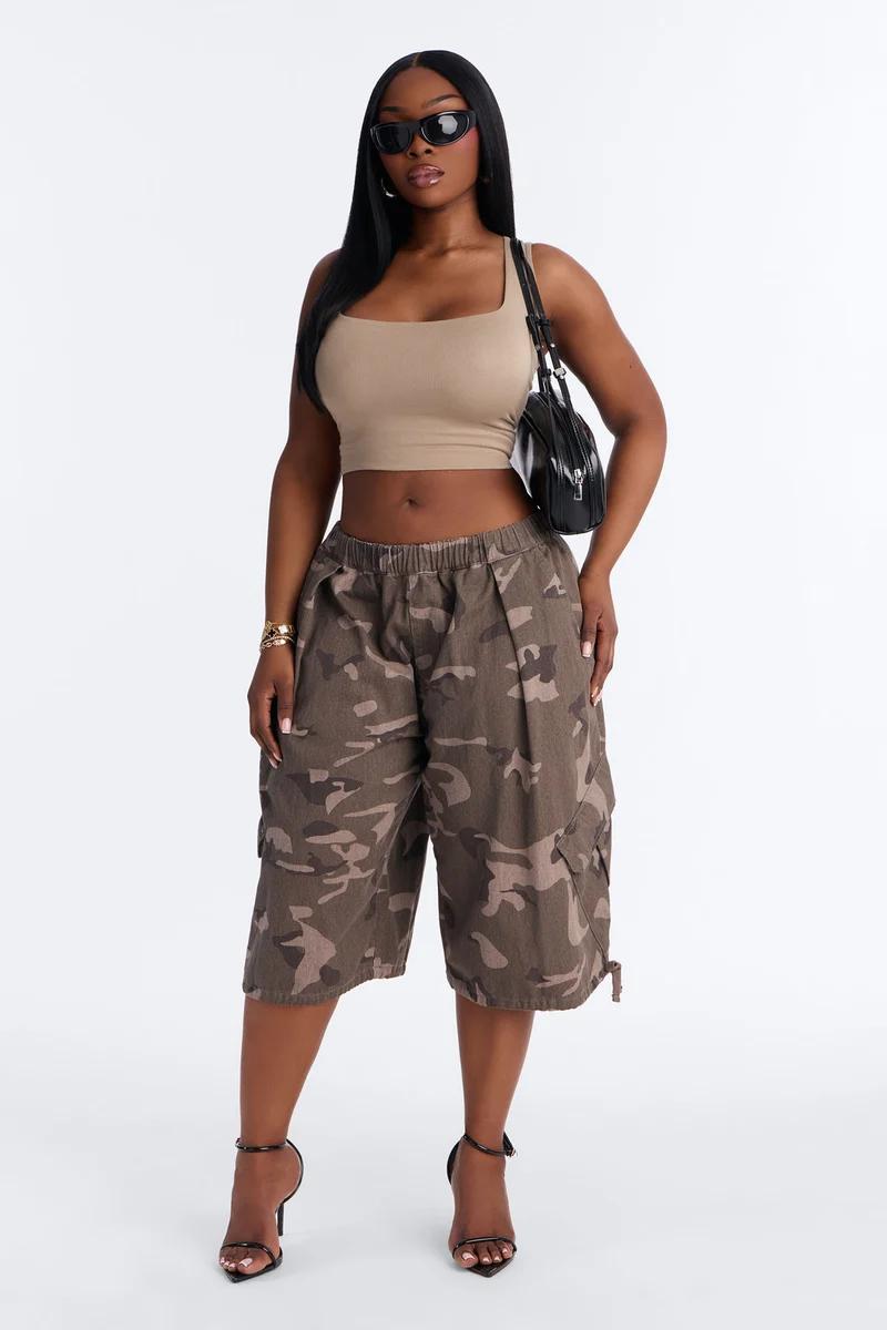 Woman posing in a beige crop top and camouflage cargo shorts with heels, showcasing a trendy women's summer streetwear fashion outfit.