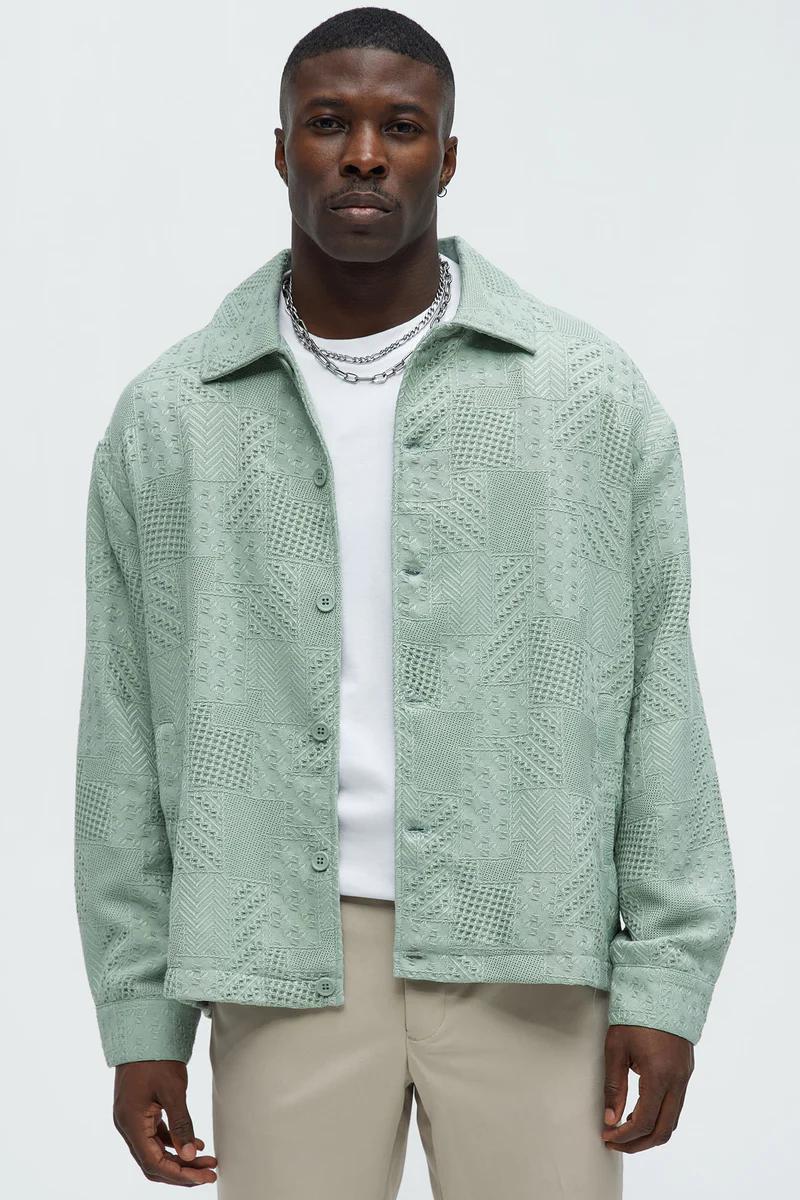 Man modeling a mint green textured button-up overshirt with geometric patterns over a white tee and beige pants. Shop men's fashion.