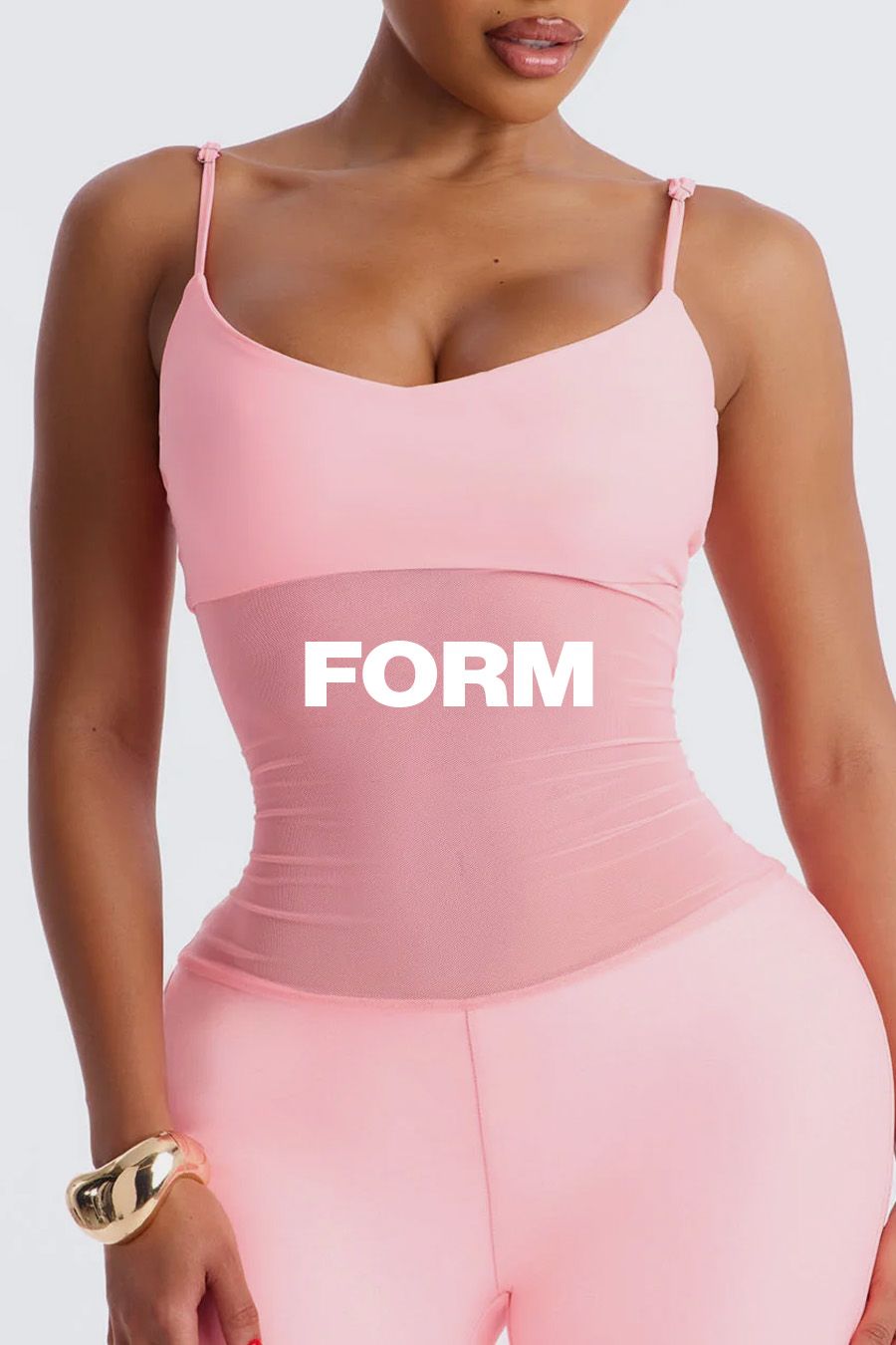 Dark-skinned woman in a pink form-fitting activewear bodysuit with a sheer mesh waist, featuring "FORM" text. Promotes shaping fashion.