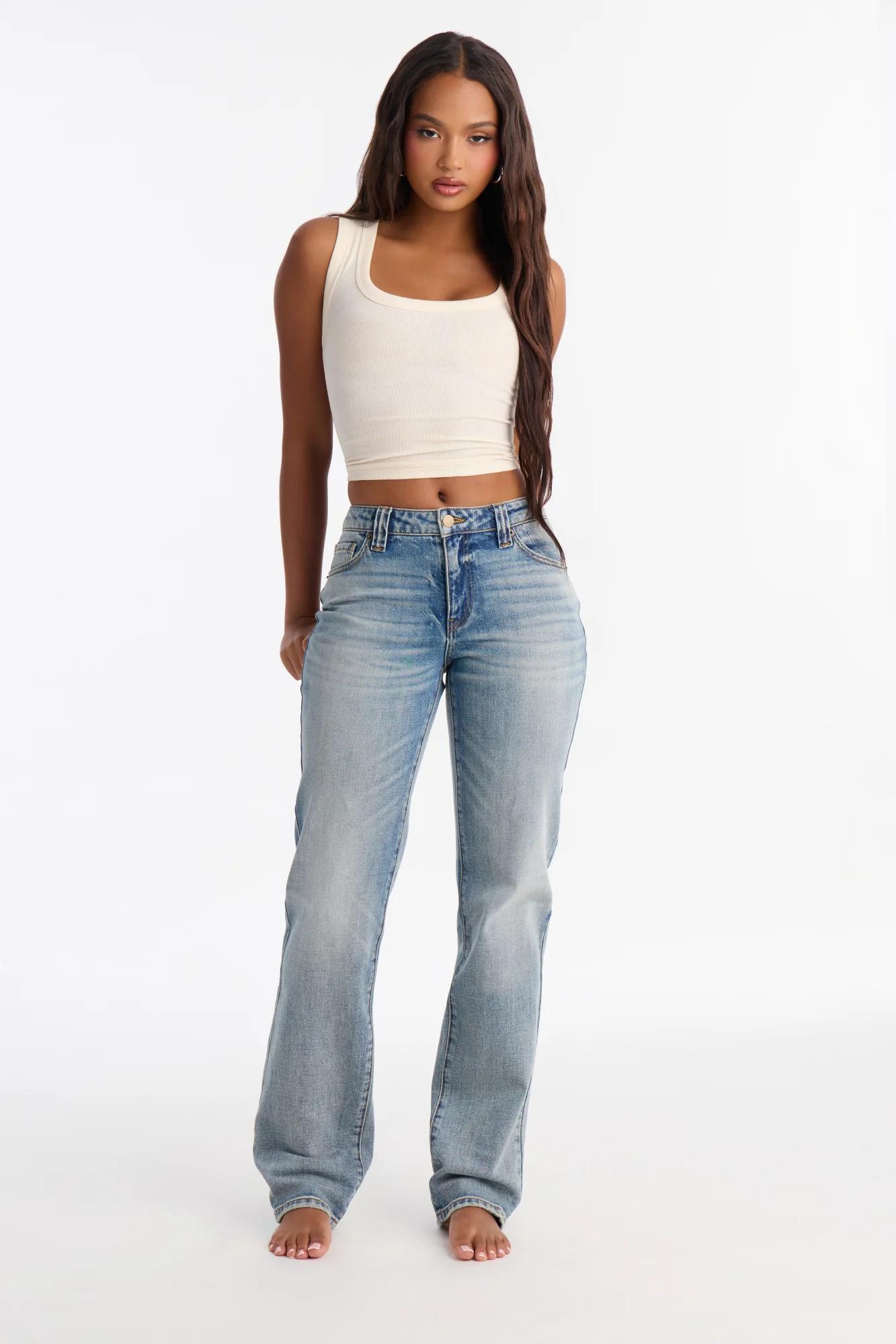Mujer con top corto blanco y jeans de tiro alto claros, mostrando un estilo casual moderno de la nueva colección de ropa de mezclilla.