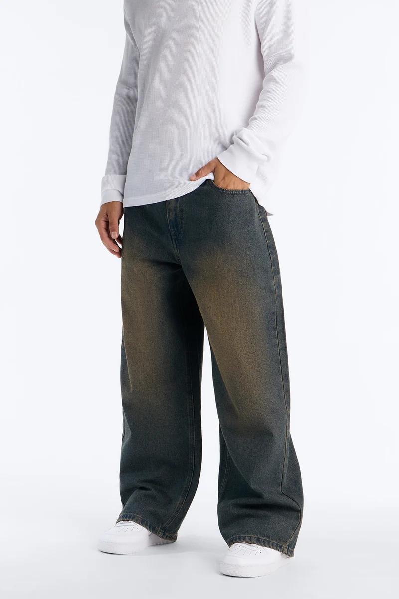 Person wearing a white long-sleeve shirt and trendy dark faded baggy jeans with hand in pocket, showcasing a new casual denim collection.