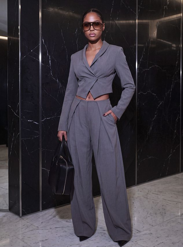 Woman in a stylish grey cropped blazer and wide-leg pants set, holding a black handbag, showcasing the new chic fall collection.