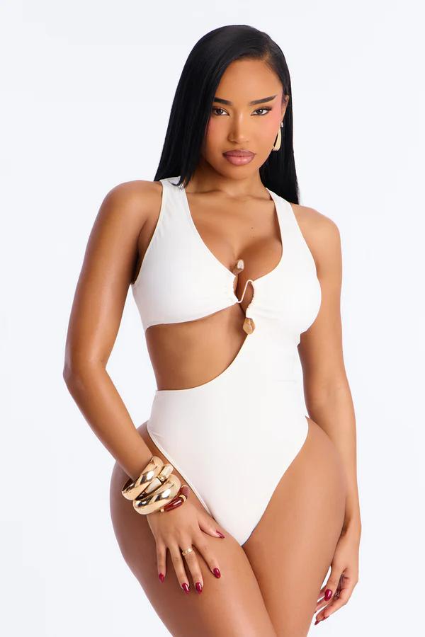 Woman modeling a chic white one-piece swimsuit with cutout details and gold ring hardware, showcasing elegant swimwear fashion.