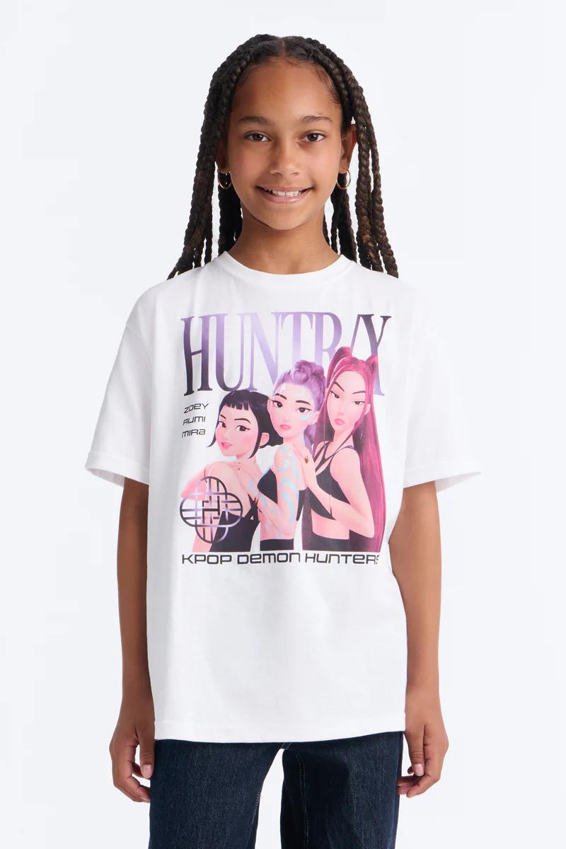 Smiling girl in white K-Pop "HUNTRAY Demon Hunter" graphic tee.