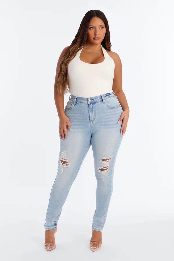 Modelo de talla grande posa con body halter blanco y vaqueros pitillo de tiro alto rotos en lavado claro de la nueva colección de verano.