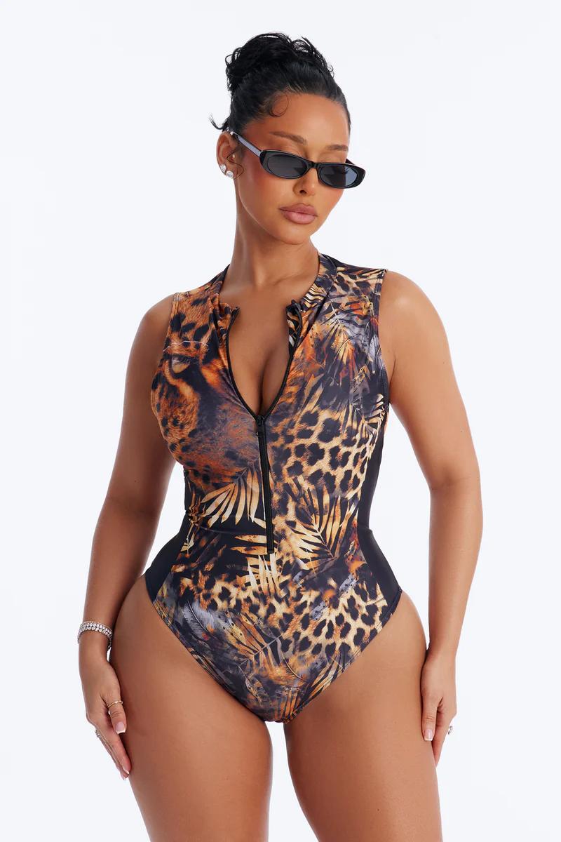 Confident woman models a chic sleeveless zip-front swimsuit: leopard & tropical print one-piece. Woman in trendy swimwear & sunglasses.