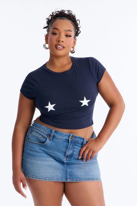 Woman in a navy crop top with two white stars and a light blue denim mini skirt, posing confidently against a white background.