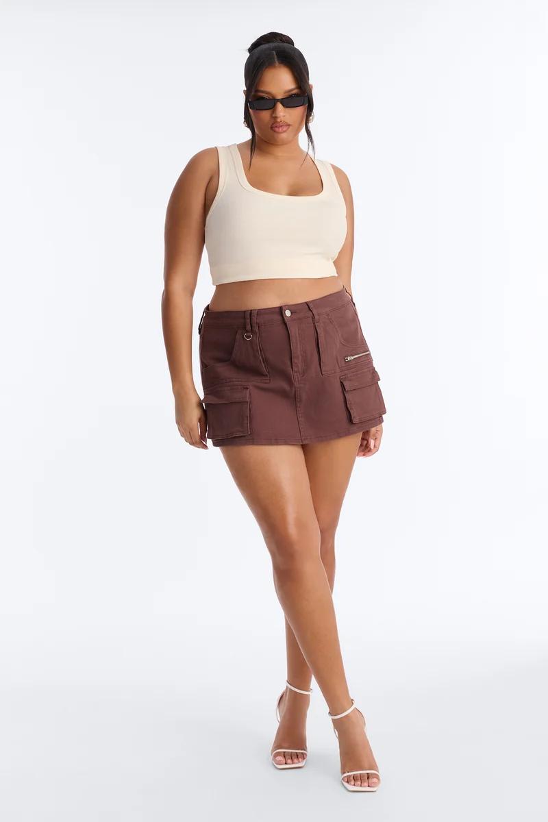 Modelo de talla grande luce un top corto crema, minifalda cargo marrón y tacones blancos, mostrando moda urbana para una colección de verano.