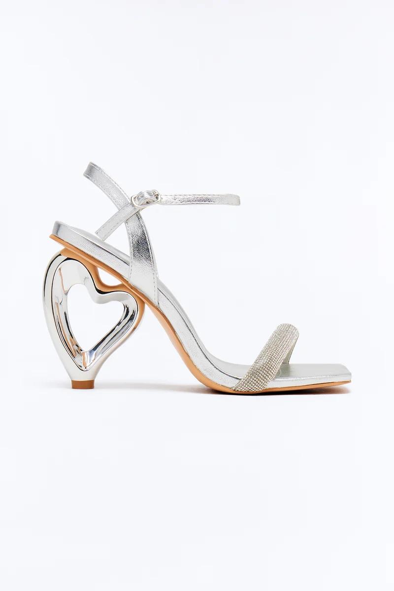 Silver metallic high heel sandal featuring a unique heart-shaped heel and a sparkly rhinestone front strap.
