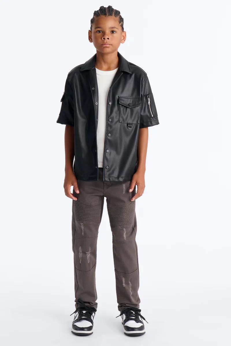 Boy in black faux leather shirt, white tee, distressed grey biker pants. Kids fashion, streetwear.