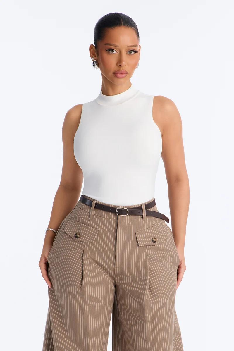 Mujer con un top blanco de cuello alto sin mangas y pantalones de rayas marrones de pernera ancha.