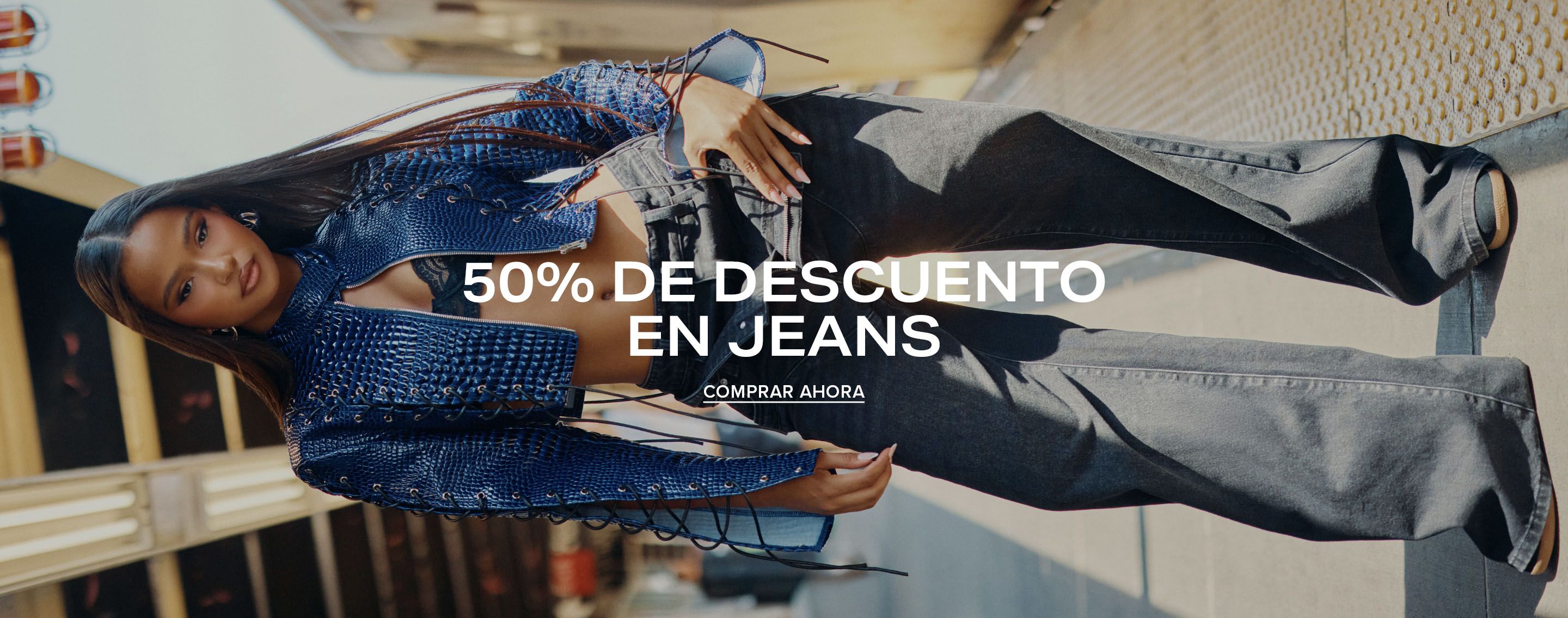 Mujer con vaqueros negros de pernera ancha y chaqueta corta azul en una estación de metro. Texto: 50% de descuento en vaqueros, compra ya.