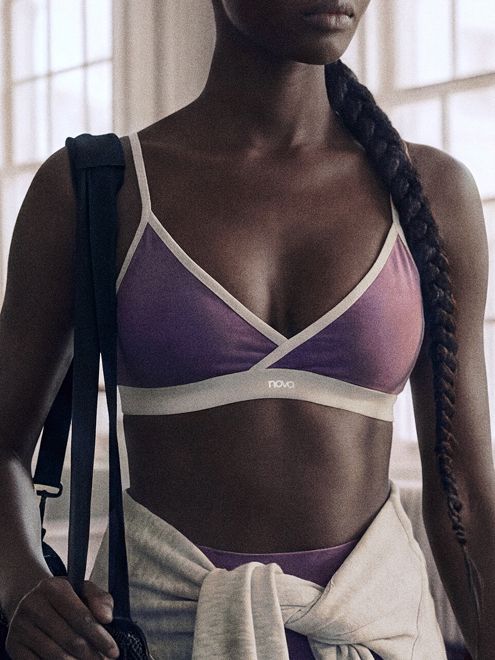 Purple Nova sports bra with cream trim and tied grey hoodie on a woman carrying a bag, promoting versatile, comfortable activewear.