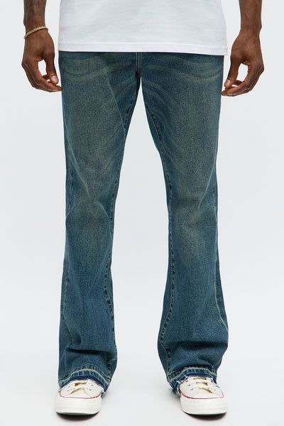 Person modeling classic blue, faded wash flared jeans with a white t-shirt and sneakers. Highlighting new men's bootcut denim style.