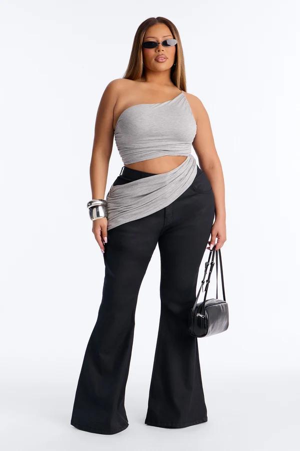 Plus size model wears a grey one-shoulder crop top and high-waisted black flare jeans, showcasing a trendy casual outfit style.