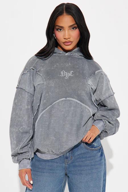 Woman models a muted pink Von Dutch zip-up hoodie and matching sweatpants with torn knees. White graphics adorn the sleeves.