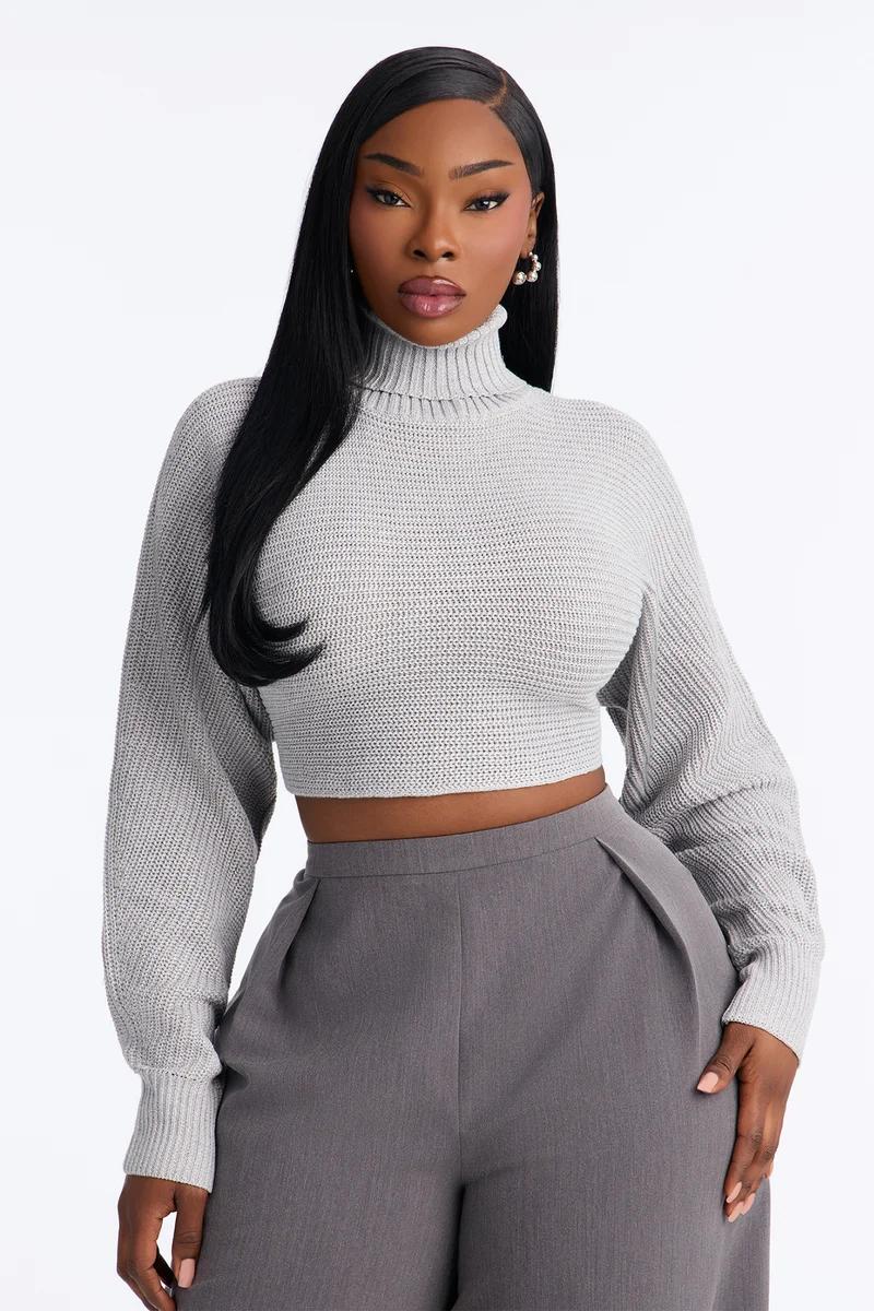 Black woman in a grey cropped turtleneck knit sweater and wide-leg trousers.