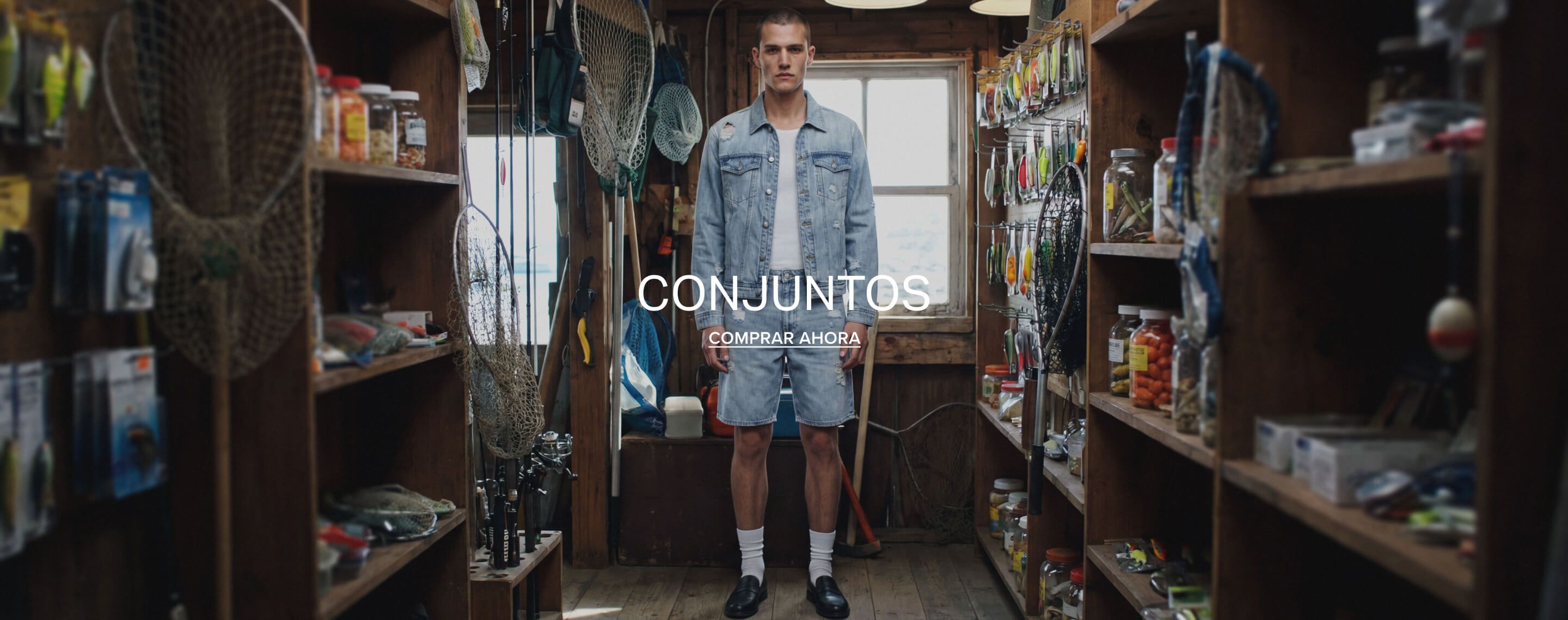 Hombre en conjunto de chaqueta y shorts vaqueros desgastados azul claro en tienda de pesca, promocionando nuevos atuendos casuales.