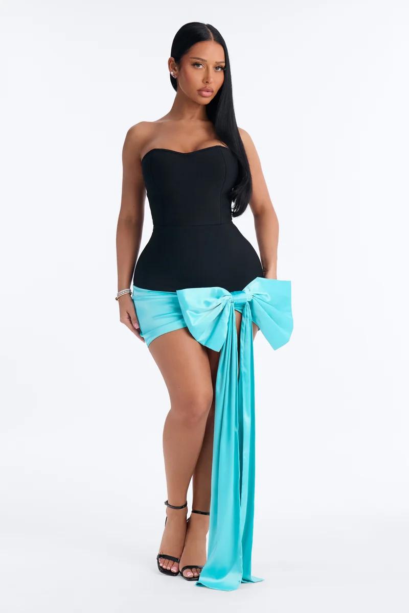 Woman wearing a black strapless mini dress featuring a vibrant cyan satin oversized bow, showcasing a glamorous cocktail party collection.