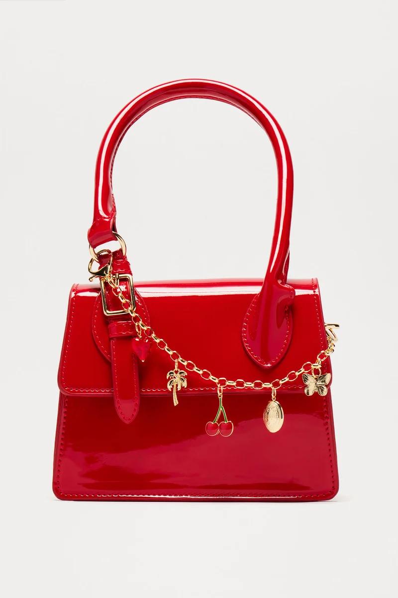 Glossy red patent leather handbag with a gold charm chain featuring cherries, a palm tree, and a butterfly.