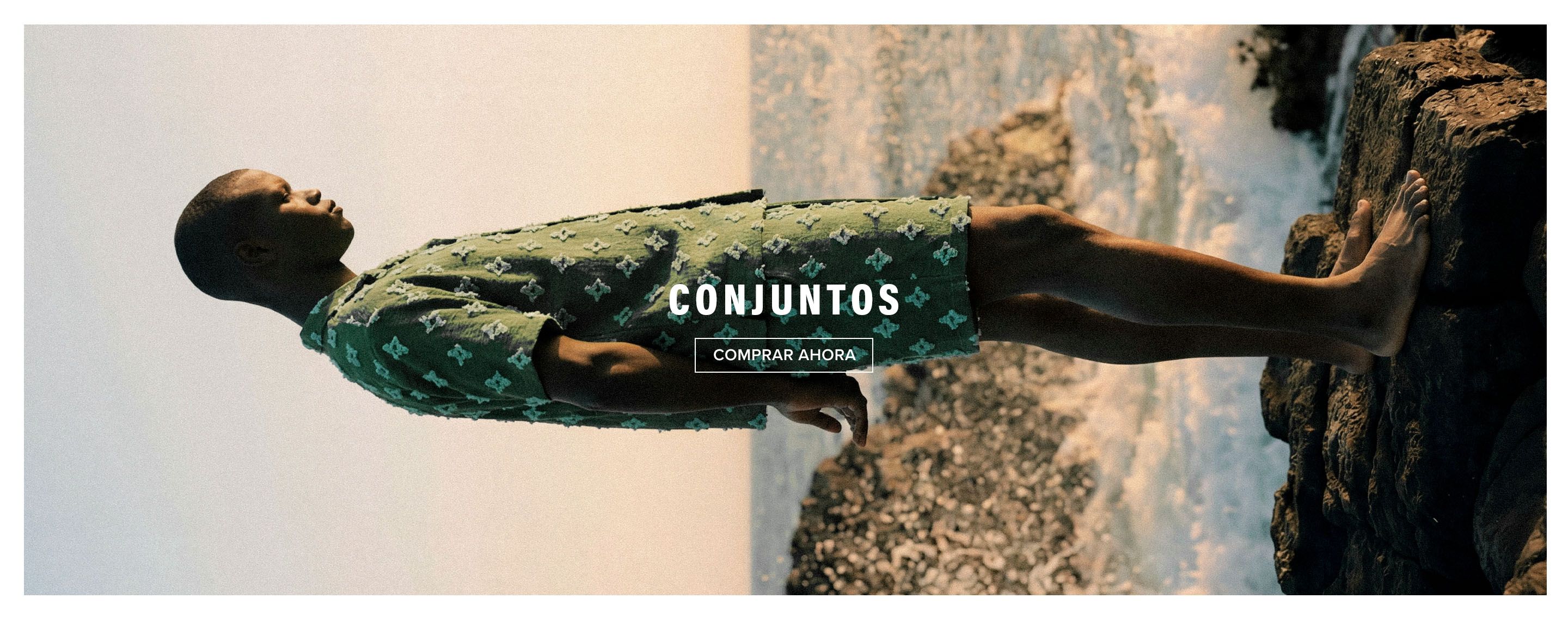 Hombre con conjunto verde texturizado de camisa y pantalón corto a juego junto al mar. Compra nuevos sets de verano para hombre ahora.