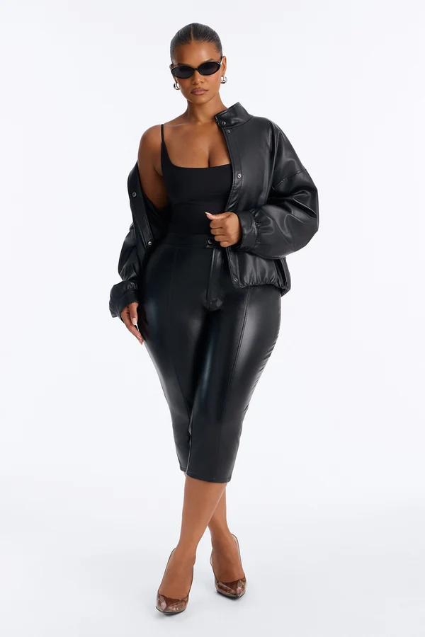 Model in a stylish black faux leather jacket and cropped pants against a white backdrop, promoting a trendy chic winter fashion collection.