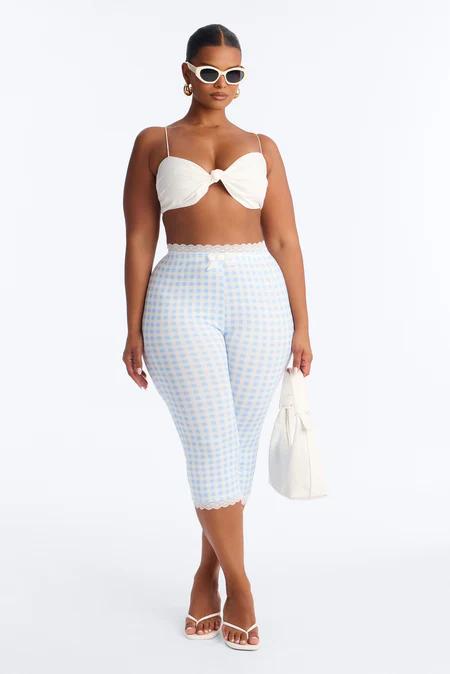 Mujer elegante posa con top blanco, leggings capri vichy azul y encaje, sandalias blancas, gafas de sol, y bolso a juego.