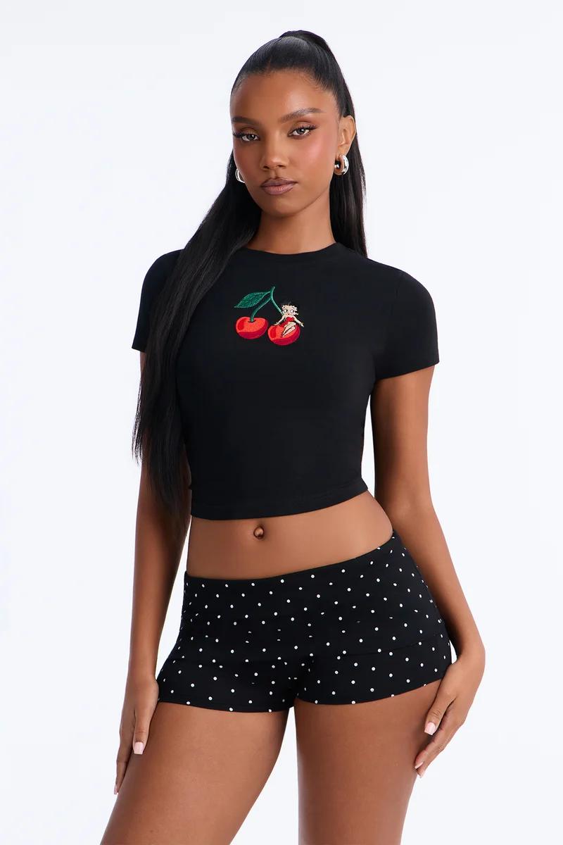 Woman wearing a black short-sleeve crop top with a cherry graphic and black polka dot shorts.