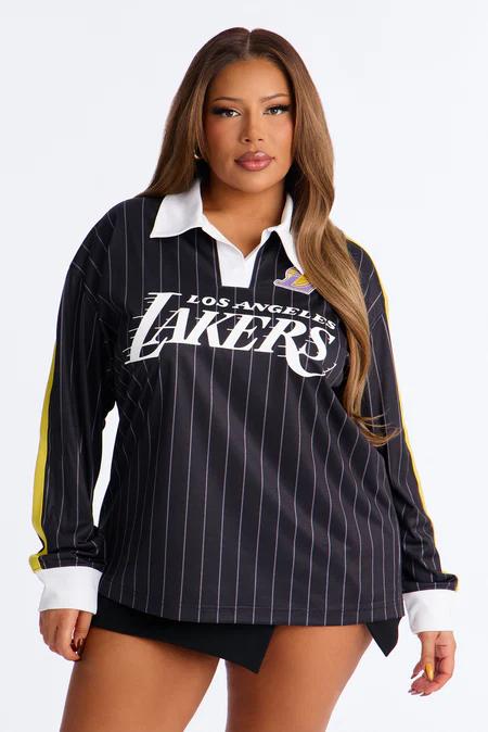 Mujer posa en polo manga larga negro a rayas de Los Angeles Lakers, con cuello, puños blancos y franjas amarillas en mangas.