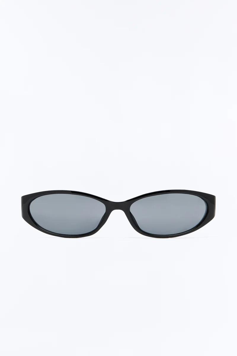 Gafas de sol ovaladas negras con lentes oscuras sobre fondo blanco, destacando un diseño retro y minimalista de la nueva colección de moda.