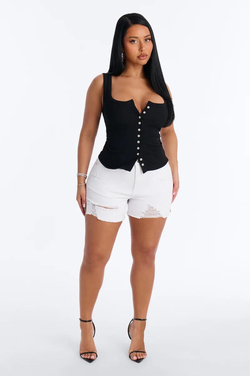 Woman wears a black sleeveless button-down top and distressed white denim shorts, showcasing a casual and trendy summer fashion outfit.