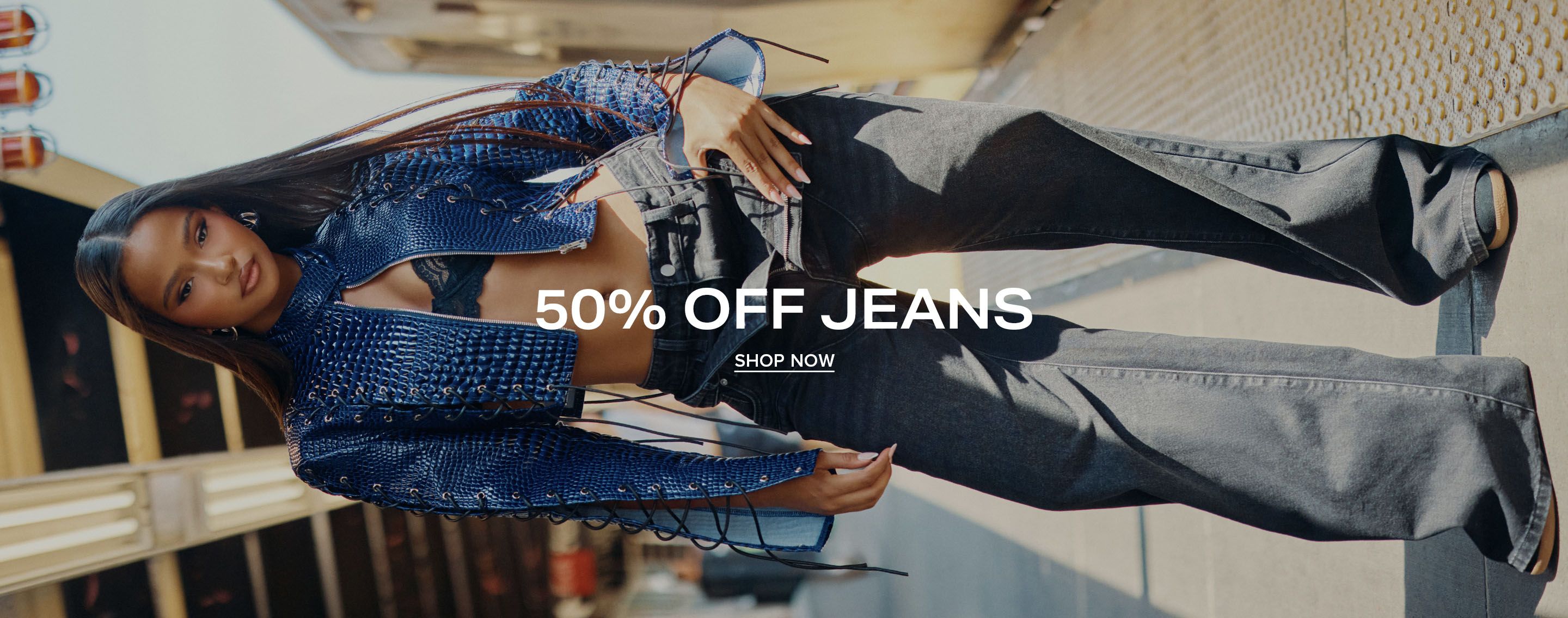 Woman in stylish wide-leg black denim jeans and a blue cropped jacket at a subway station. Text overlay: 50% off jeans, shop now.