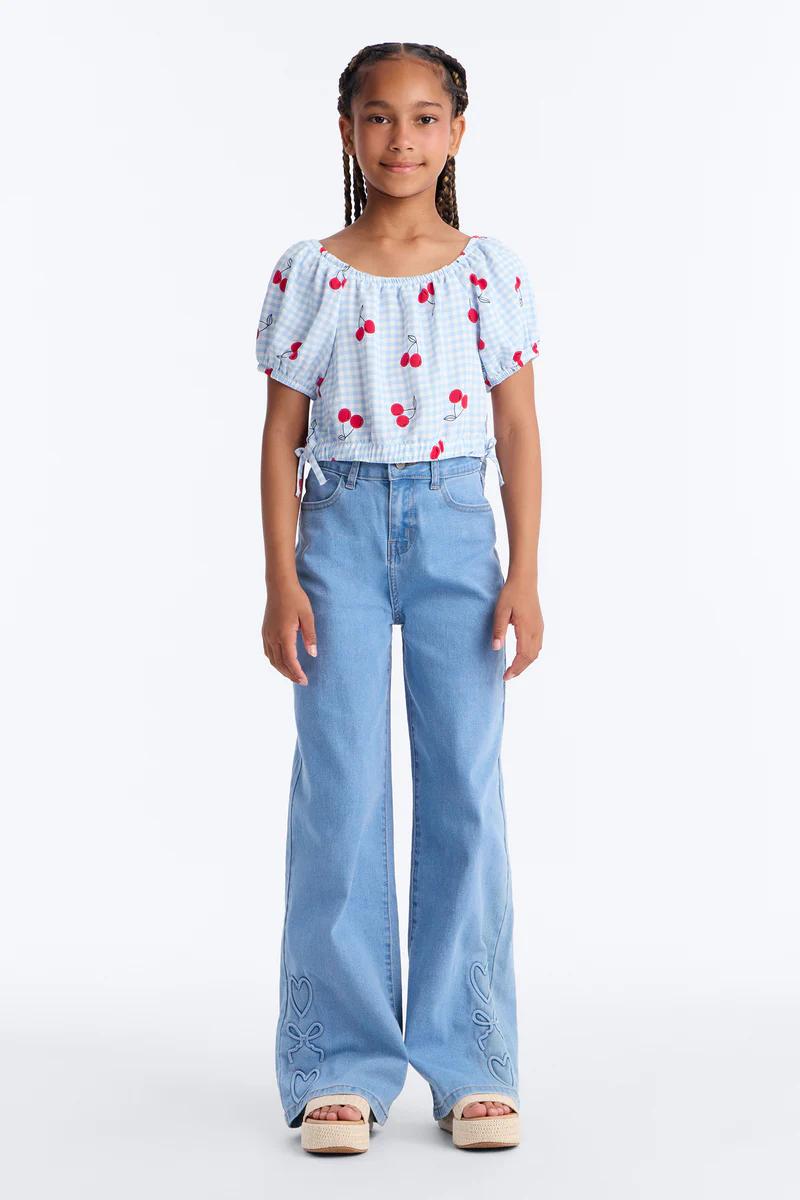Young girl in cherry print gingham crop top, wide-leg embroidered jeans, and platform sandals.