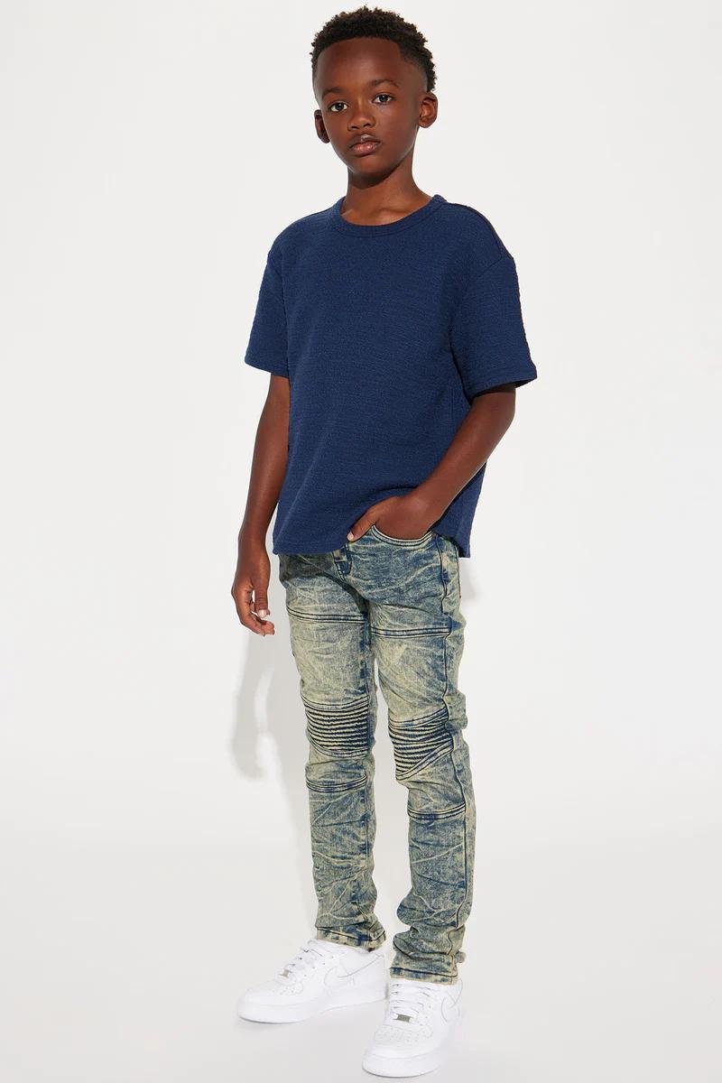 Young boy in navy blue textured t-shirt, acid wash moto jeans, & white sneakers. Kids fashion outfit.