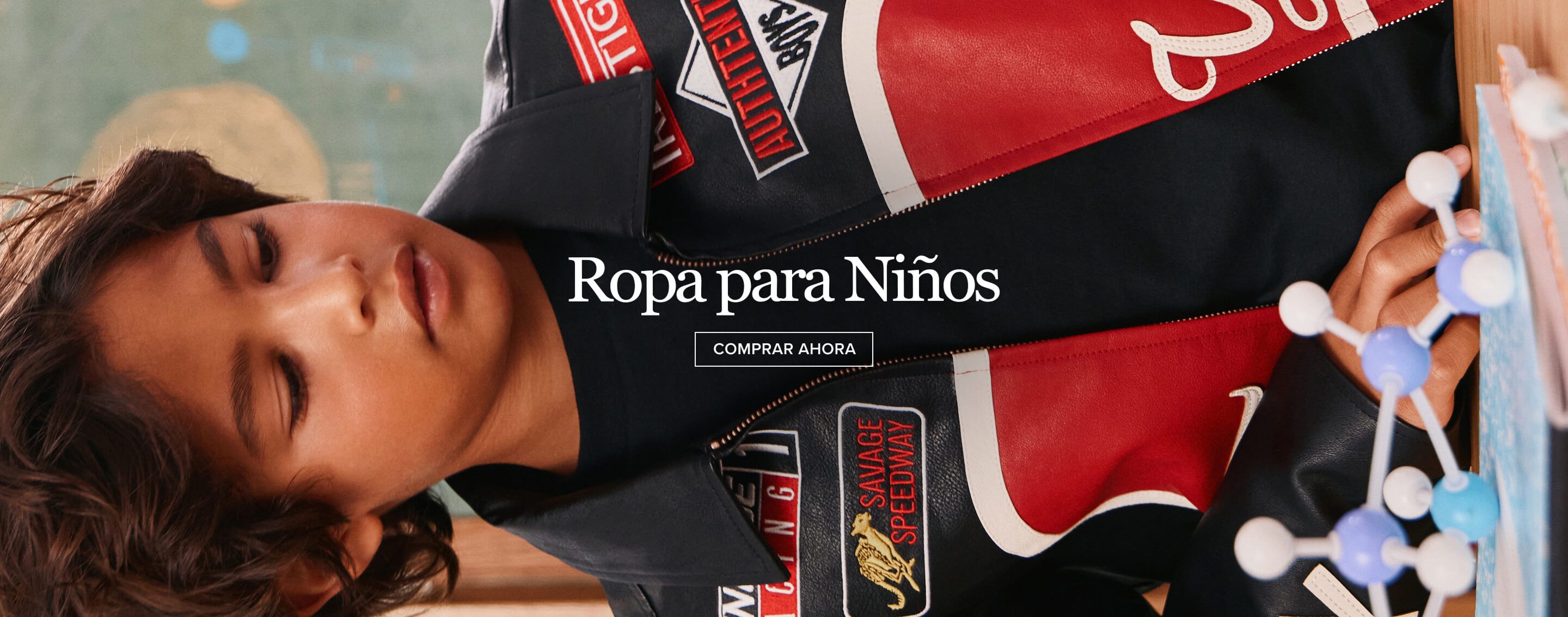Niño con chaqueta de carreras negra, roja y blanca con parches, mirando un modelo molecular. Compra moda infantil masculina.