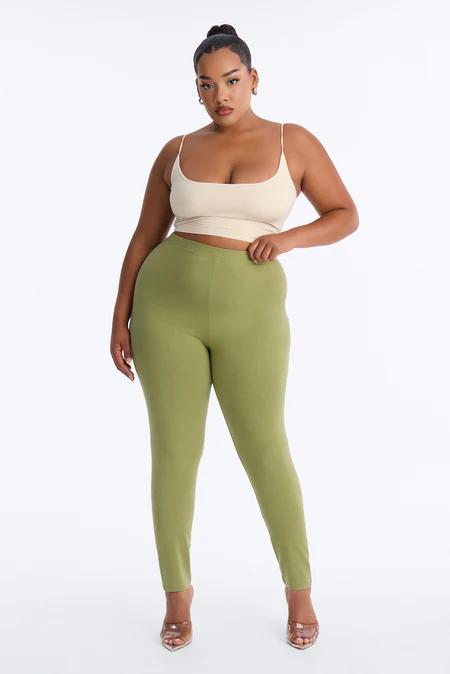 Mujer de talla grande de cuerpo entero con top corto beige, pantalones verde oliva de tiro alto y tacones marrones. Fondo blanco.