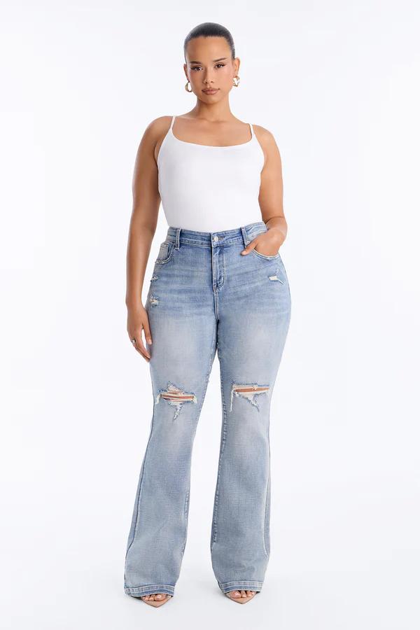 Modelo de curvas con jeans de campana rotos en lavado claro y un body de tirantes blanco, promoviendo moda casual de talla grande.