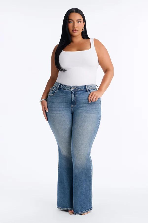 Modelo de talla grande luce jeans acampanados de tiro medio azul y top blanco de tirantes, destacando moda vaquera en catálogo de estudio.