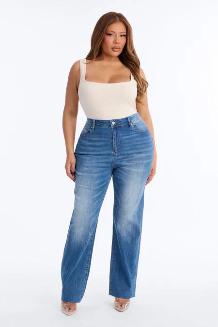 Mujer con cabello castaño largo con top beige de cuello cuadrado, jeans azules anchos de talle alto y tacones puntiagudos oro rosa.