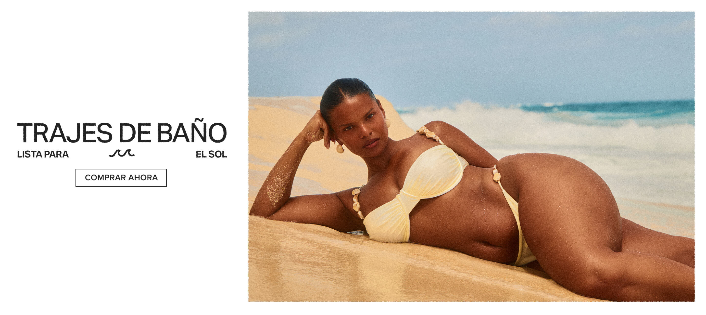 Modelo en bikini amarillo con detalles de conchas sentada en playa de arena con el océano y olas detrás. Explora nuestra nueva colección de baño.