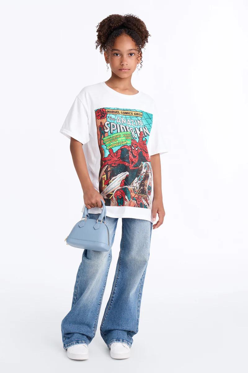 Niña con camiseta de cómic Spider-Man, jeans anchos, zapatillas blancas y bolso azul.