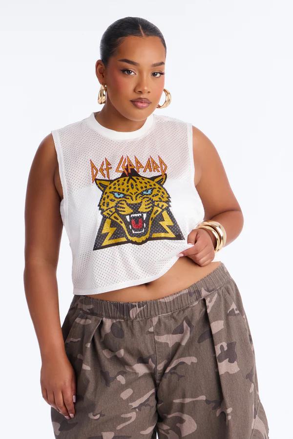 Mujer en top corto blanco de malla con leopardo Def Leppard y pantalones camuflaje. Con aros y pulseras doradas, mira al frente.