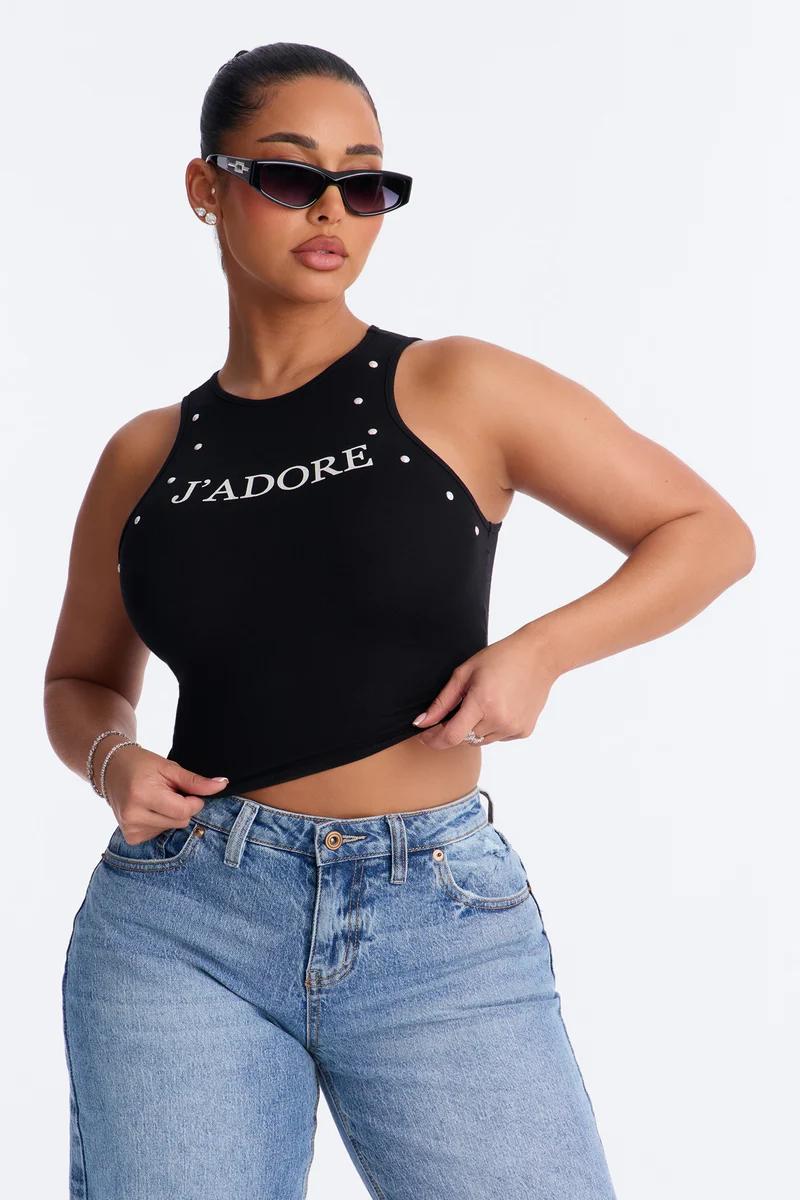 Mujer con top negro sin mangas de J'adore con tachuelas y vaqueros azules.