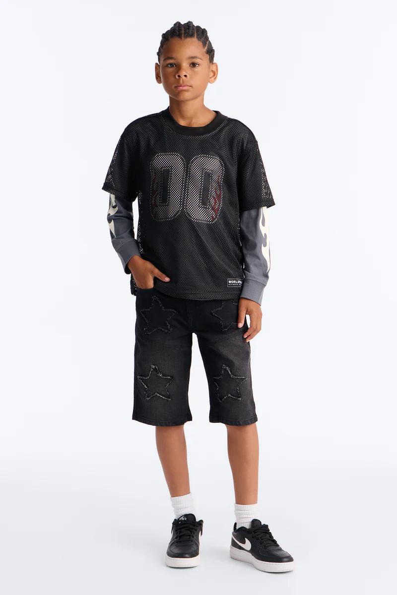 Young boy in black mesh '00' jersey, flame long-sleeve, star denim shorts, and black sneakers. Trendy kids' streetwear fashion.