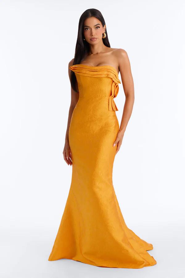 Elegant woman modeling a shimmering rose pink off-shoulder gown with a ruched, fitted bodice and flowing mermaid skirt, holding a silver clutch. Ideal formal wear.