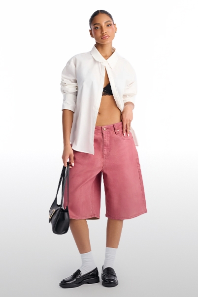 Model wears open white oversized shirt, black bra, dusty rose denim culotte shorts, black loafers & bag. Showcasing new summer collection.